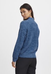 Pull en tricot bleu avec un col montant et des manches longues, présentant un tissu texturé et une coupe décontractée.