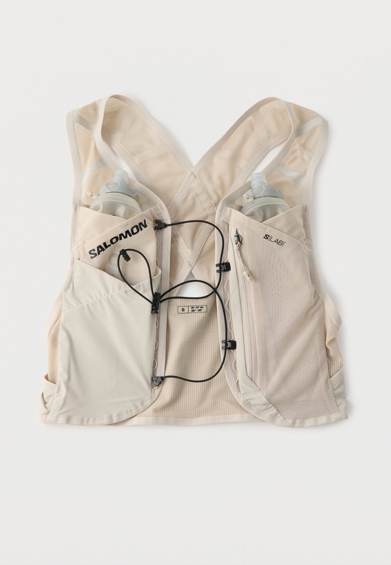 Gilet d'hydratation de course Salomon beige clair avec dos en maille, cordons ajustables à l'avant, deux poches pour bouteilles d'eau et une poche zippée latérale.