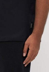 Sort bomuld t-shirt med korte ærmer, diskret sømtag på siden mærket "CORE," glat tekstur, tætsiddende design og uden synlige mønstre.