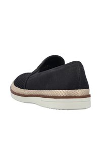 Zapato negro sin cordones con parte superior texturizada, detalles en beige trenzado alrededor de la suela y suela de goma blanca.