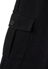 Tissu noir de manteau avec une poche latérale et une fermeture à bouton. Texture lisse avec un design ajusté et des détails de couture subtils.