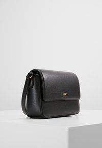 Borsa a tracolla in pelle nera con chiusura a patta, hardware dorato e logo impresso. Design compatto con tracolla e superficie texturizzata.