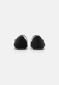 Black woven flat shoes with a textured surface, round toe, and open back design. Features adjustable ankle strap and minimal hardware.