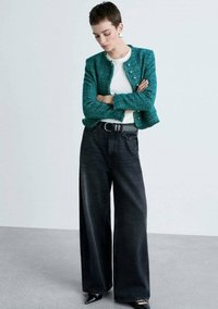Giacca in tweed turchese con bottoni dorati, t-shirt bianca e jeans neri a vita alta e a gamba larga. Tacchi neri a punta completano il look.