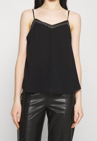 Top negro sin mangas con escote en forma de V y adornos de perlas decorativas a lo largo del escote, hecho de una tela suave y ligera.