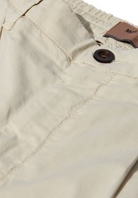 Lyse beige bomuldsbukser med en glat tekstur, der har en brun knap og synlige syninger nær taljen.