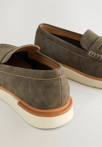 Grå suedet slip-on sko med en rund tå og stikninger, der har en beige gummisål og en glat, struktureret overflade.