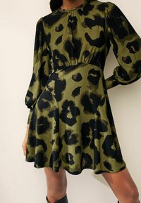 Robe à imprimé léopard vert et noir avec un tissu texturé, des manches longues, une taille élastique et un ourlet évasé.