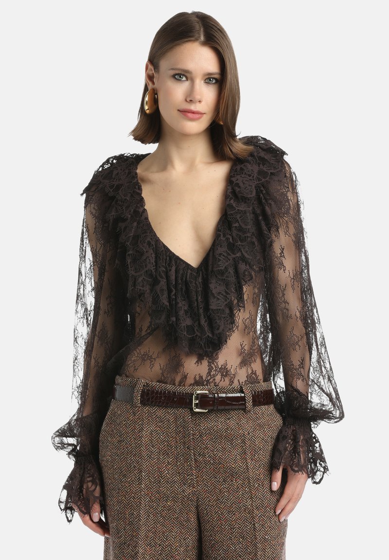 Zwarte kanten blouse met een diepe V-hals, ruches bij de hals en mouwen, gedragen over bruine houndstooth broeken en een bruine ceinture taille.