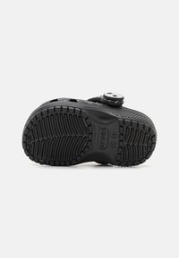 Black rubber clog with textured sole, featuring a round, adjustable strap at the top and small ventilation holes for breathability.