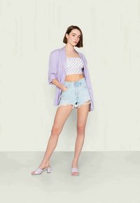Blazer oversized em lavanda, top cropped branco com bolas, calções desgastados em azul claro e sandálias de salto bloco em lavanda.