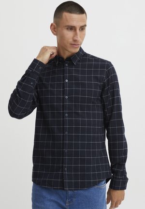 Mørkeblå ternet skjorte med knapper og hvide gitterlinjer, lange ærmer og krave; stoffet virker let og tekstureret.