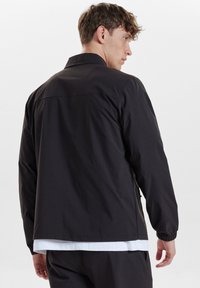 Černá lehká bunda s límečkem, elastickými manžetami a rovný střih. Má hladký povrch a minimalistický design.