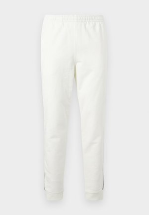 Pantalon de survêtement blanc à taille élastique, avec chevilles resserrées et coutures latérales discrètes, présenté sur un fond clair uni.
