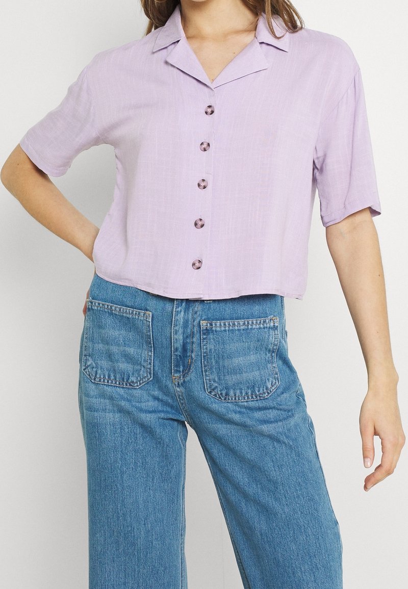 Lila kortärmad skjorta med krage och sex runda knappar framtill. Matchad med högmidjade blå denimjeans.