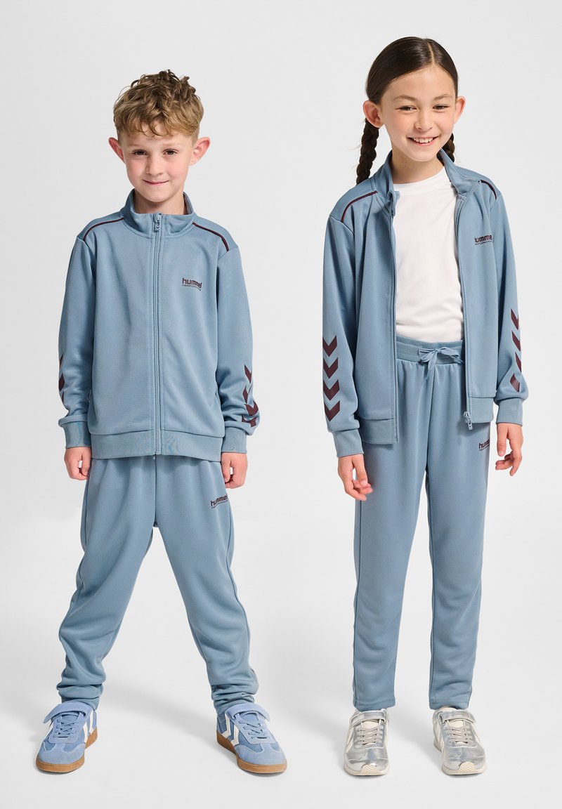 Niebieskie dresy z czerwonymi akcentami, z kurtką na zamek i spodniami z elastycznym pasem, wykonane z gładkiego materiału. W zestawie dziecięce obuwie sportowe.