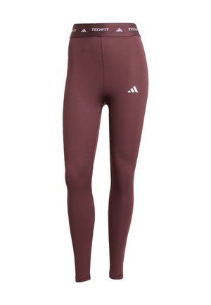 Bordové legíny s přiléhavým střihem. Mají široký pas s nápisem "TECHFIT" a třemi bílými pruhy jako akcenty na boku. Hladká textura.