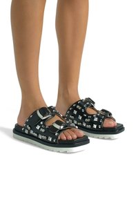 Sandali neri con borchie quadrate e accessori in argento, caratterizzati da una spessa suola bianca, design con apertura per le dita e cinturini regolabili.