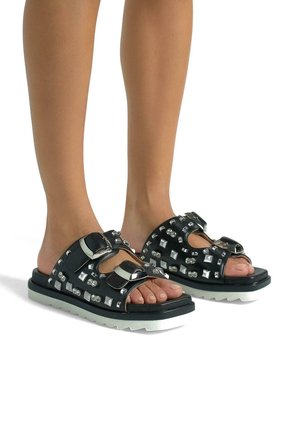 Sandali neri con borchie quadrate e accessori in argento, caratterizzati da una spessa suola bianca, design con apertura per le dita e cinturini regolabili.