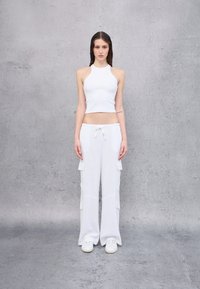 Weißes geripptes Halter-Crop-Top kombiniert mit weißen Cargo-Hosen mit Seitentaschen und verstellbarem Bund, ergänzt durch weiße Sneakers.