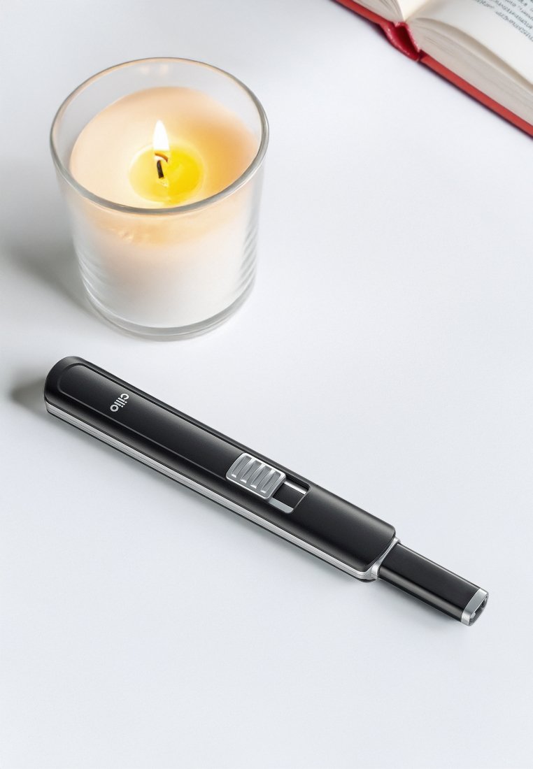 Schwarzer Kerzenanzünder mit elegantem Design, Metallknopf und gebogenem Auslass, platziert neben einer Glaskerze auf einer hellen Oberfläche.