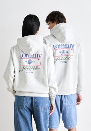 Gray hooded sweatshirt featuring "tommy jeans" graphic in blue and green with established date and location printed on the back.