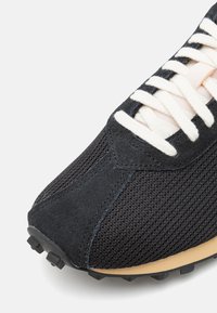 Svarta mesh-sneakers med mockadetaljer, vita snören, texturerad tåhatt och en gummisula med greppande punkter.