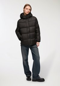 Czarna pikowana kurtka z kapturem, z przodu z zatrzaskami i bocznymi kieszeniami. Noszona z luźnymi dżinsami i czarnymi butami.