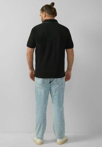 Schwarzes Poloshirt mit kurzen Ärmeln, kombiniert mit hellblauen Jeans. Das Shirt hat einen strukturierten Kragen und einen lässigen, lockeren Schnitt.