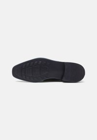 Suola di una scarpa da uomo in pelle nera con battistrada testurizzato e tacco leggero, mostrata su uno sfondo bianco semplice.