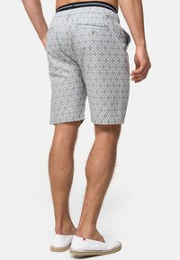 Shorts gris à motifs avec un design géométrique, une taille élastique et un détail de poche arrière. Le matériau semble léger et respirant.
