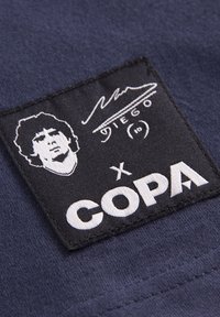 Parche de tela azul marino con retrato impreso en blanco, firma y el texto "COPA" con un acento estilizado en forma de "x".