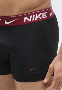Μαύρα αθλητικά μποξέρ με ελαστική μέση σε μαρόν χρώμα, διακοσμημένη με "NIKE" σε λευκό και μικρό κόκκινο λογότυπο Nike στο πλάι.