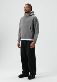 Grijze hoodie met een zak aan de voorkant, gecombineerd met zwarte wijd uitlopende jeans en zwarte schoenen met gekleurde veters. Eenvoudig, sportief ontwerp.