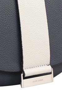 Dettaglio di una borsa in pelle blu navy con tracolla bianca. Materiale texturizzato, hardware in argento e accento di marca aggiungono un'eleganza funzionale.