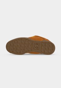 Semelle d'une basket orange avec une semelle extérieure en caoutchouc brun texturé et un logo de marque embossé au centre.