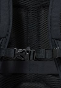 Zaino in tessuto nero con schienale in rete strutturata, dotato di spallacci regolabili, fibbia di plastica e cinturini piatti per una chiusura sicura.