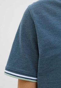 Donkerblauwe polo met een gestructureerde stof. Heeft korte mouwen met een witte en groene gestreepte manchetdetail.
