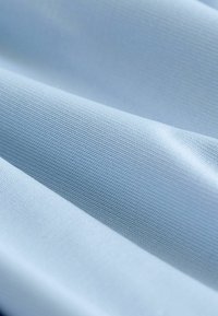 Jasnoniebieska teksturowana tkanina o gładkim, tkanym wzorze, z subtelnymi różnicami w odcieniu i głębokości w wielu zagięciach.