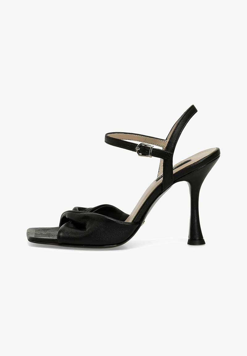 Musta korkokengät sandaalit, joissa on kierrerakenteinen varvasremmi, säädettävä nilkkaremmi ja hoikka stiletto-korko. Liukas viimeistely.