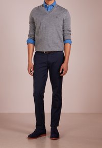 Grå v-ringad tröja över en ljusblå skjorta med knappar, tillsammans med marinblå byxor och marinblå mockaskor med bruna sulor. Minimalistisk design.