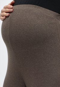 Καφέ κολάν με απαλό, υφασμένο ύφασμα και εφαρμοστό σχέδιο, που τονίζει το στρογγυλό σχήμα και τη ψηλή μέση.