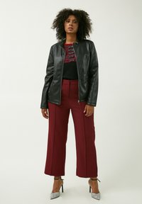 Giacca in finta pelle nera con colletto a coste, abbinata a pantaloni larghi a vita alta in bordeaux e scarpe con tacco argento. Maglione strutturato sotto.