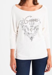 Weißes Strickoberteil mit weitem Ausschnitt, Dreiviertelärmeln, floralem Grafikdruck und verziertem Schriftzug "Guess USA 1981 Washed Jeans".