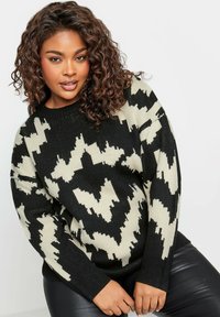 Maglione a strisce nere e crema con un design in maglia texturizzata, caratterizzato da un collo rotondo e maniche lunghe, abbinato a pantaloni neri eleganti.