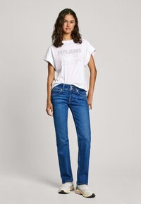 Camiseta blanca con un estampado gráfico, jeans rectos azules y zapatillas blancas con acentos en rosa y gris. Look simple y casual.