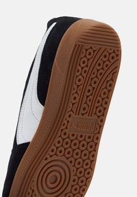 Baskets noires et blanches avec une tige en daim, une semelle en gomme caoutchoutée et un motif de semelle circulaire. Présente un logo embossé sur la semelle.