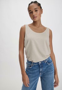 Top senza maniche beige realizzato in tessuto morbido, con scollatura a girocollo e vestibilità comoda, abbinato a jeans in denim blu chiaro.