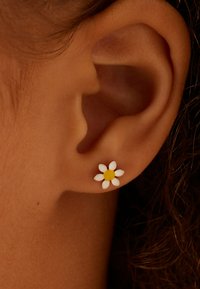 Bloemvormige oorbel met zes witte bloemblaadjes en een gele kern, gemaakt van glad materiaal, getoond aan het oor van een persoon.