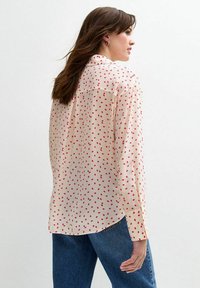 Lichte, crèmekleurige blouse met een patroon van rode stippen, lange mouwen en een licht gebogen zoom, gecombineerd met blauwe denim jeans.